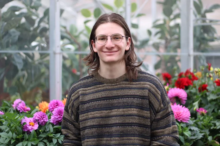 Student in greenhouse looking at camera with flowers in background
