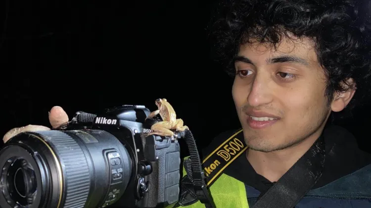 Soham looking at a small frog that is sitting on the lens of his camera.
