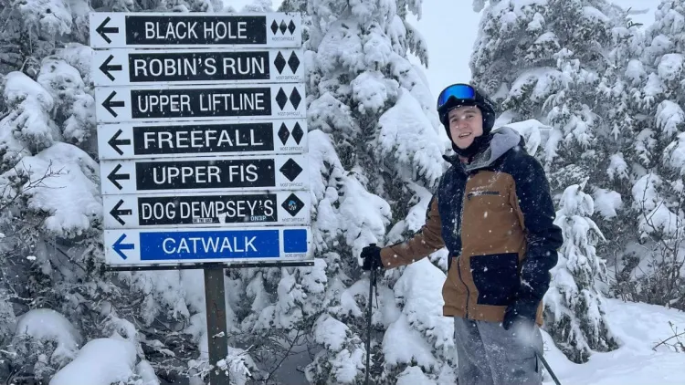 Chris posing with a sign on a snowy ski mountain.