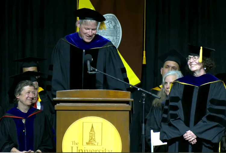 Interim Dean Allan Strong honoring Clare Ginger at the 2024 graduation celebration - both are on stage and wearing regalia