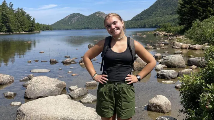 Sara standing with her hands on her hips in front of a lake with mountains in the background.