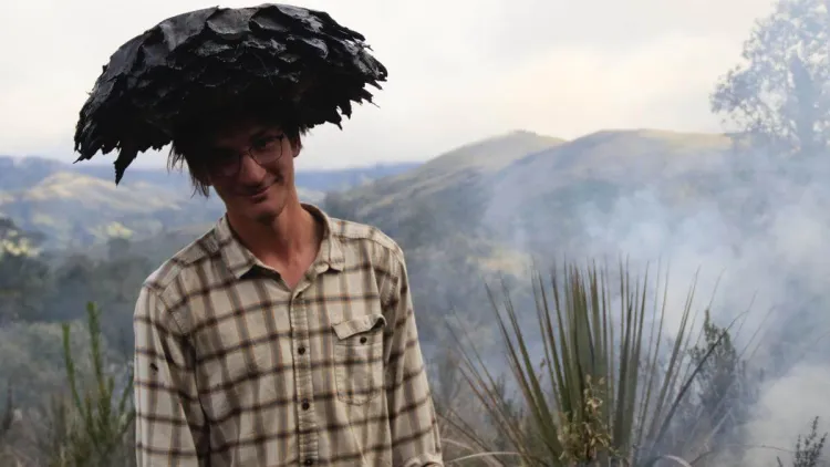 Val balancing a piece of burned tree on his head with smoky mountains in the background.