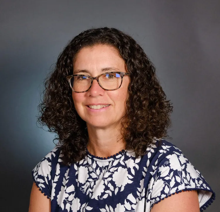 A person with curly hair and glasses wearing a flower print shirt