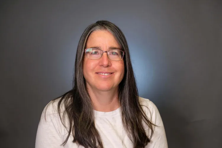 A person with long hair and glasses in a white shirt