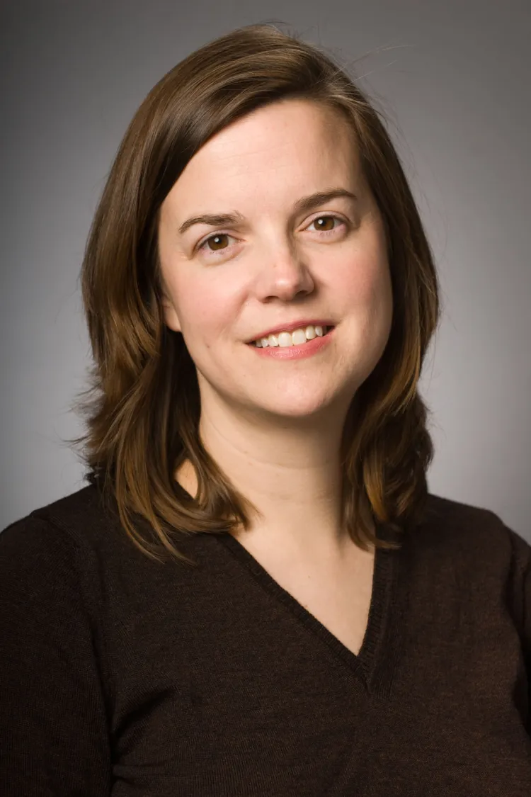 A headshot of a person with shoulder length brown hair in a black shirt