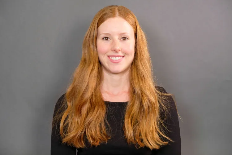 A headshot of a woman with long red hair in a black shirt