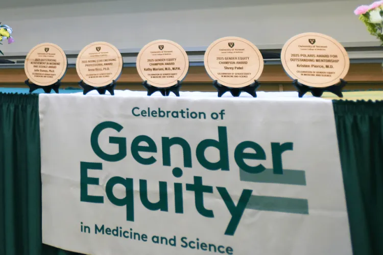 a banner for the Celebration of Gender Equity in Medicine and Science, on a table with circular wooden award plaques