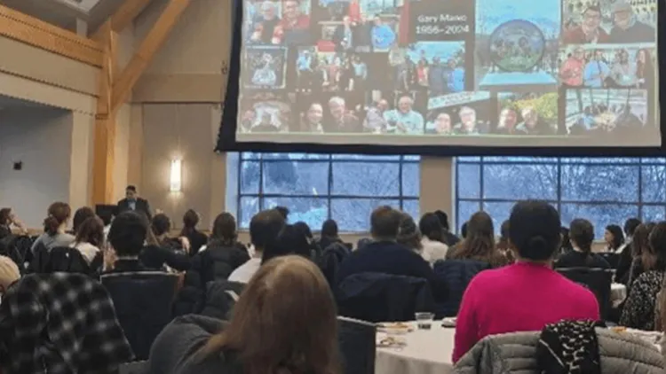 The crowd looks up at a presentation slide presented by the keynote speaker who stands at a podium at the front of the room. 