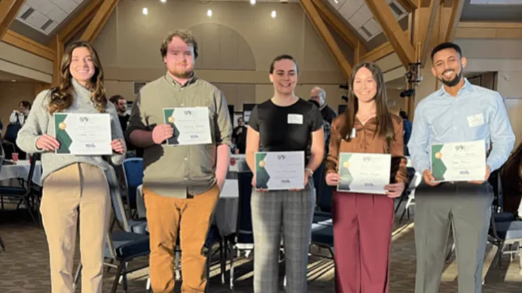 Five individuals stand in a line with certificates in their hands. 