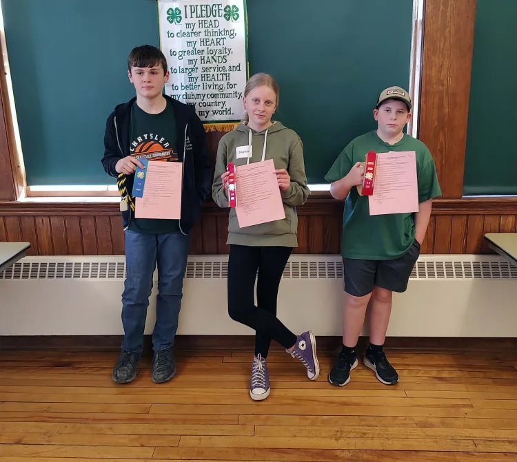 three 4-h'ers posing with certificates and ribbons