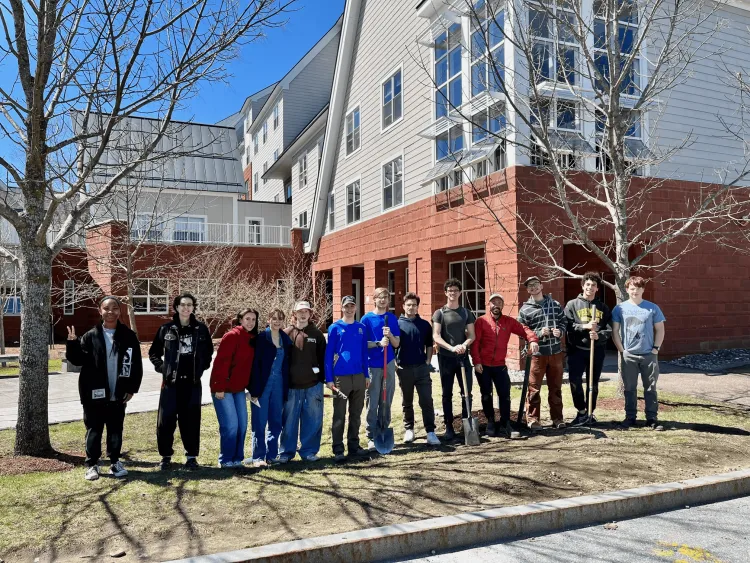Row of college students with tools for tree planting standing between trees