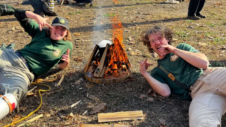 Es and a friend posing next to a campfire they built.