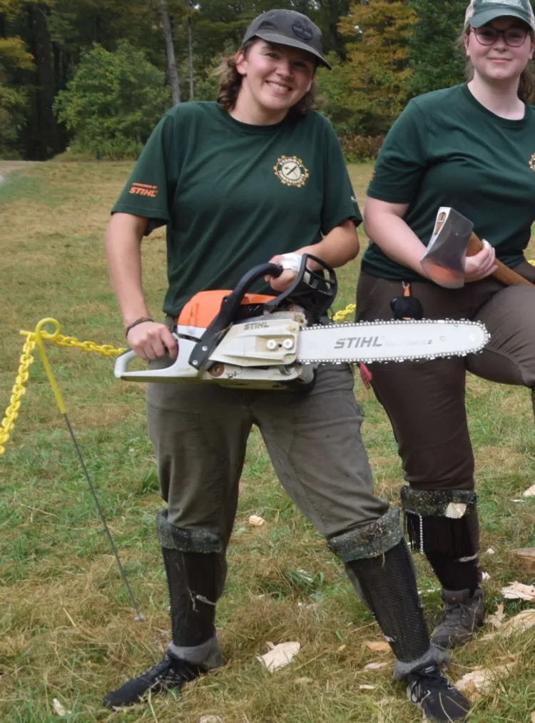 Es Sweeney holding a chainsaw and smiling with a Timbersports teammate.