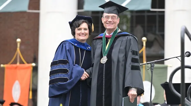 man in regalia receiving diploma from woman