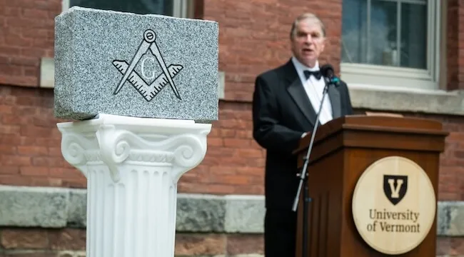 man speaking at lecturn behind ceremonial cornerstone
