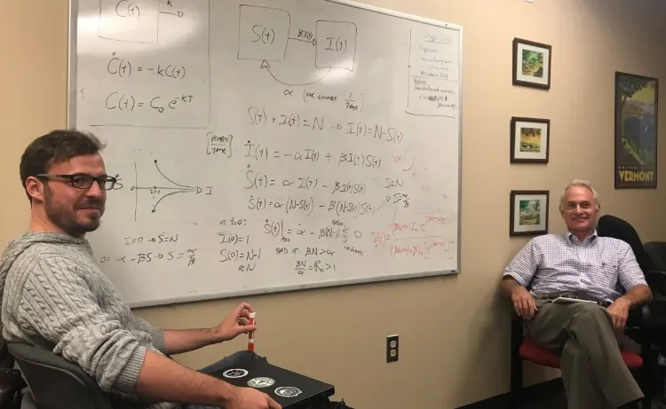 Lauent Hebert-Dufresne and Jason HT Bates sit on either side of a whiteboard covered in calculations