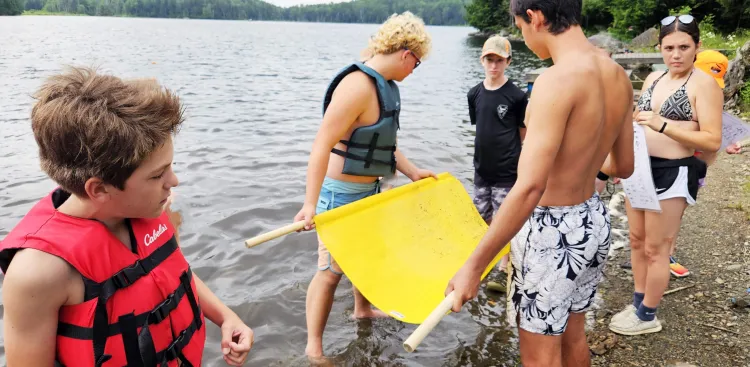 several campers examining lake water, standing at the edge of a lake