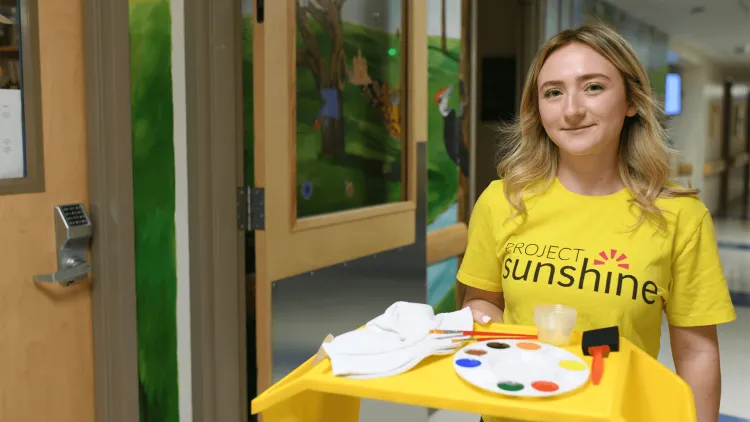 a woman carrying a tray with art supplies