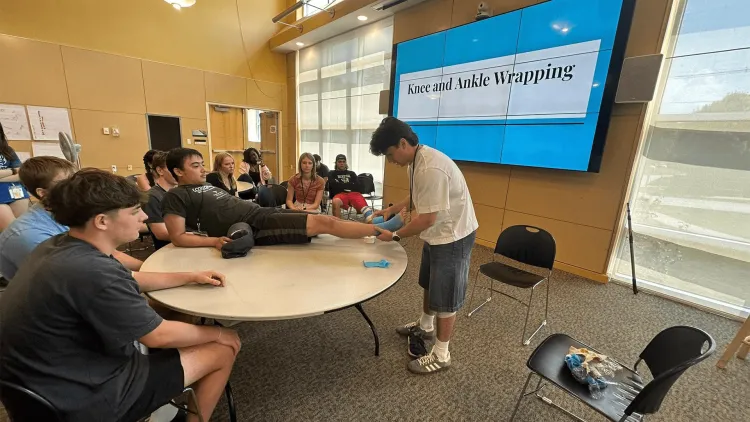 a person wrapping an ankle in front of students in a classroom