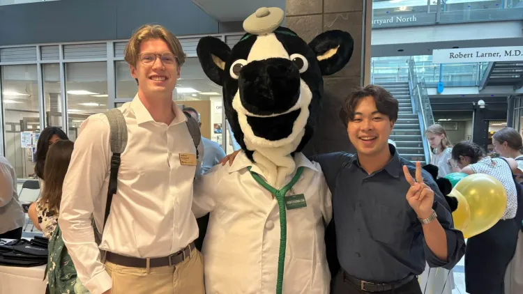 Larner mascot Dr. Moo flanked by 2 new Class of 2029 medical students