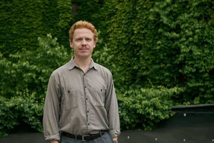 A man is standing in front of a wall of green ivy.