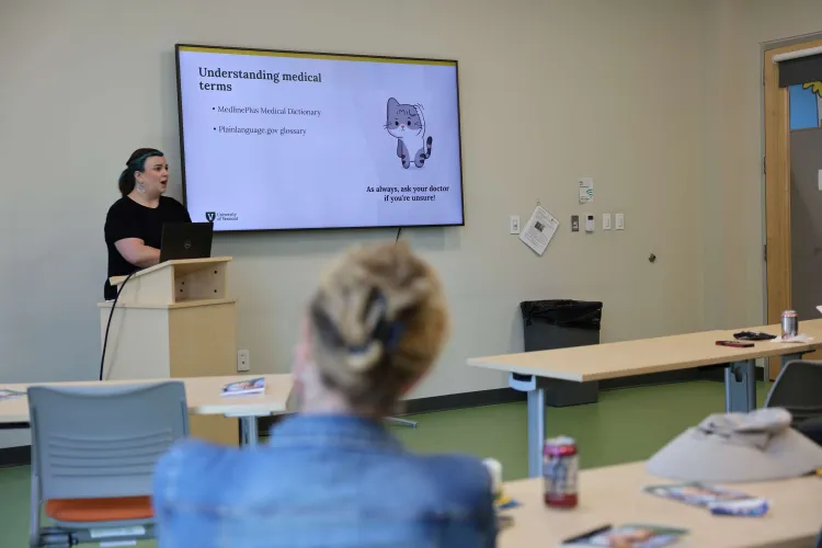 Maria Avery speaks in front of a projection screen to a group of people.