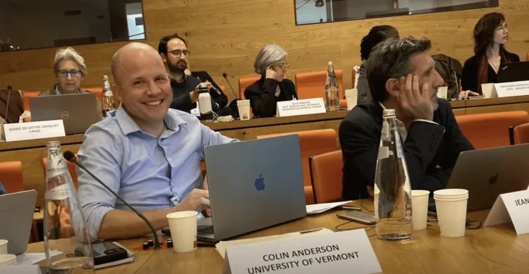 Colin Anderson sits at a table with a computer and placard with his name