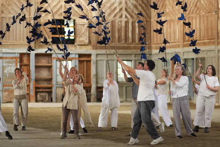 A group of dancers wearing white shirts and holding long sticks with flapping prop birds on them