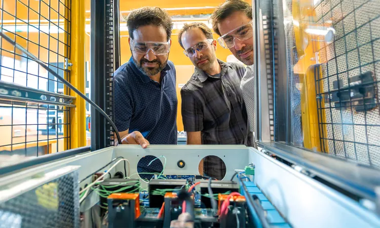 Three researchers inspect equipment in an electrical engineering lab