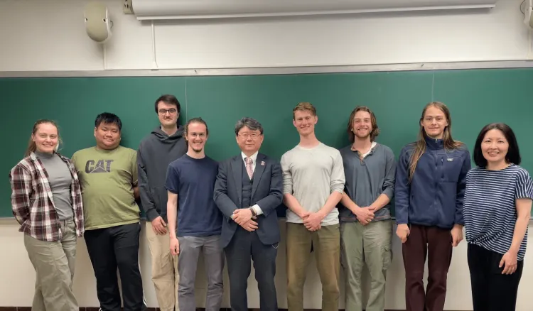 Group of eight people standing in a classroom in front of a green chalkboard, smiling for a photo