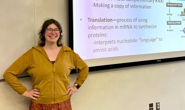 A professor posing for a photo standing next to a PowerPoint slide about the process of transcription.