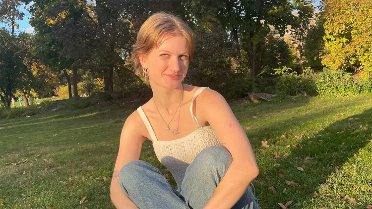 Young woman with blonde hair, white top, and jeans sitting on green lawn