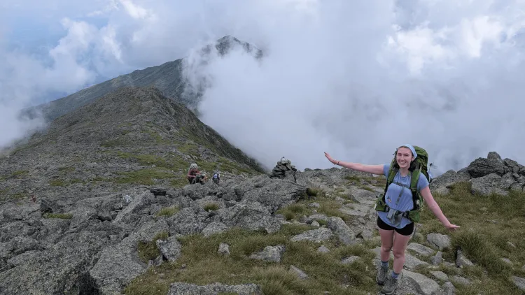 Hiker smiling on a rocky mountain ridge surrounded by clouds.