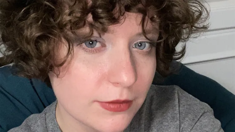 Close-up of young woman with short, dark, curly hair and gray t-shirt