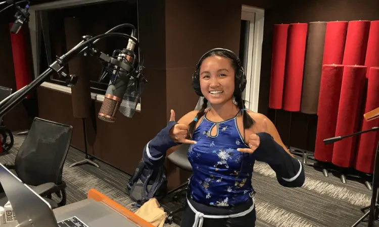 Voice actor Merk Nguyen in a recording studio wearing headphones and smiling at the microphone.