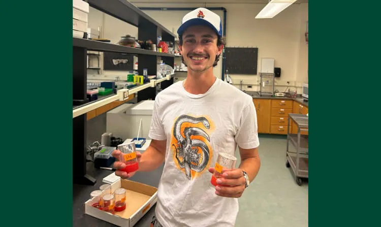 An undergraduate student in a laboratory, holding two cylinders containing fruit flies.