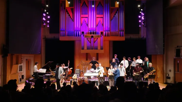 A large jazz ensemble performs on a stage lit with purple and pink light