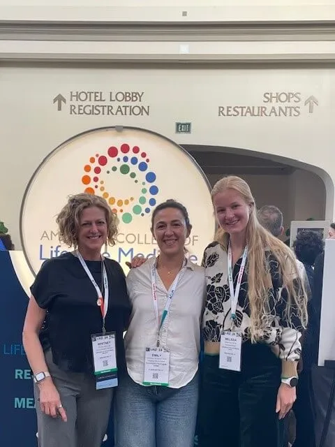 three women standing in front of a conference logo sign
