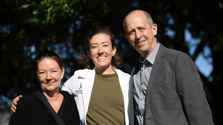 a medical student in a white coat flanked by their parents