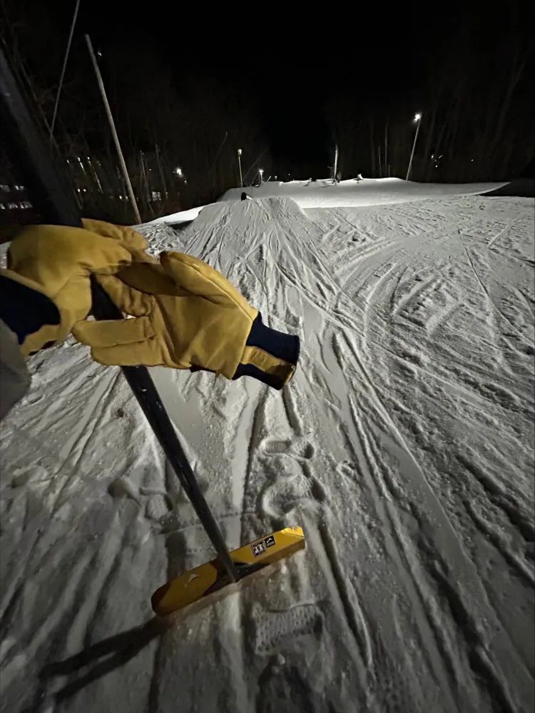 Leo holding up snow grooming equipment on a mountain at night.