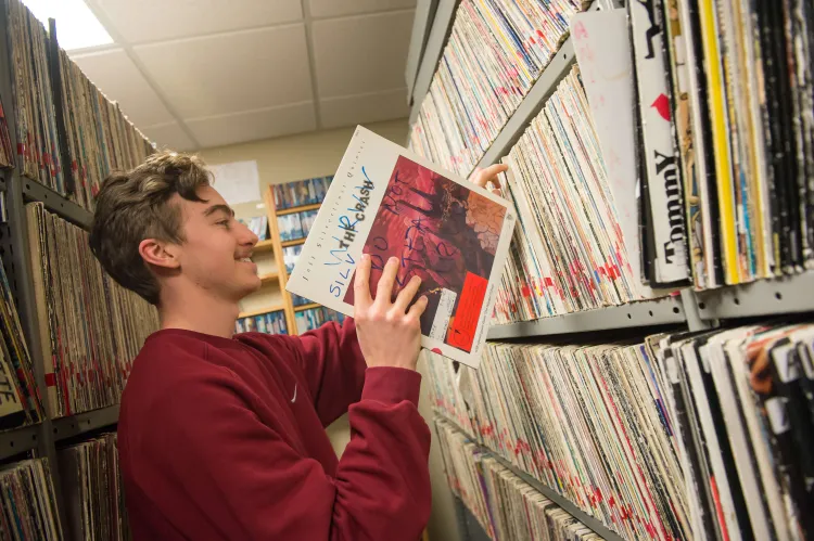 Photo of a student in a red sweatshirt putting away a record on a full shelf.