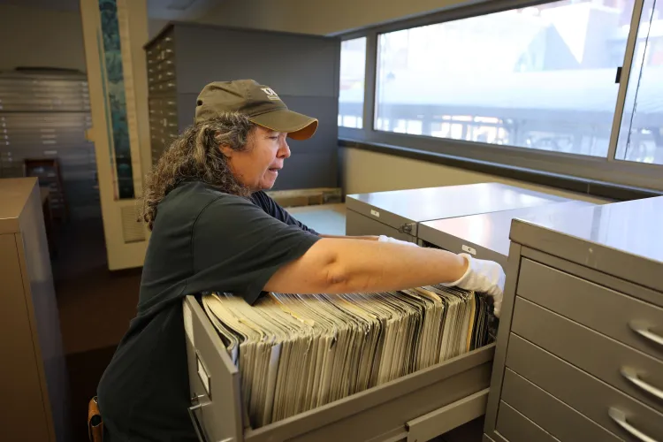 A woman flips through a file cabinet filled with aerial photos.