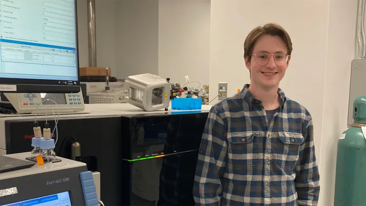 Student standing in a lab next to scientific equipment and monitors.