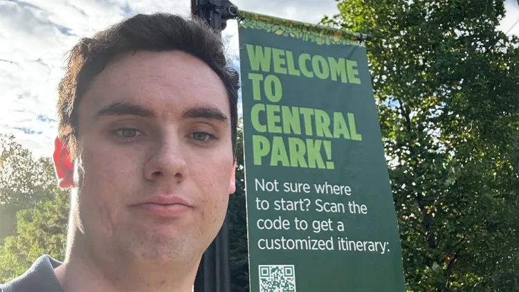 Person taking a selfie near a green “Welcome to Central Park” sign with trees and sunlight in the background.