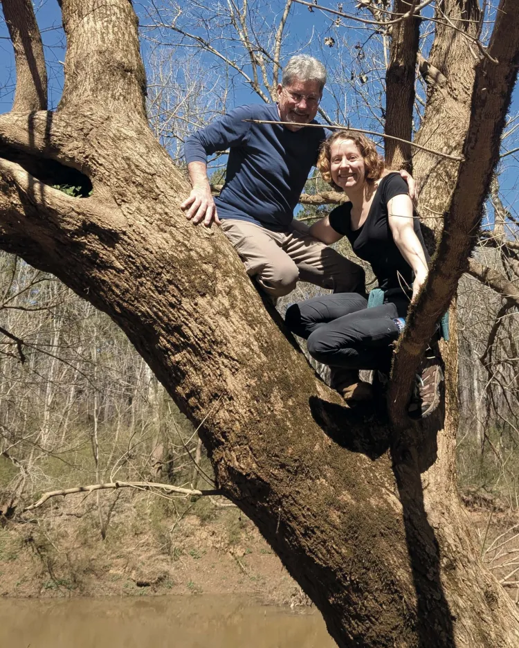 man with silver hair and his adult daughter smiling down from a large tree