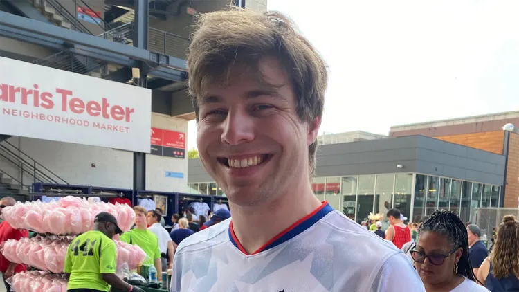 Smiling person in a white sports jersey standing outside a stadium