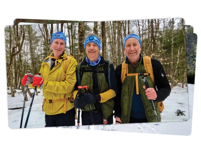 three men in winter gear with ski poles posing in the woods