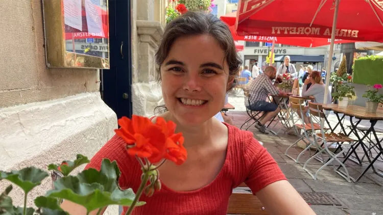 Person smiling at an outdoor café with a bright red flower in the foreground.