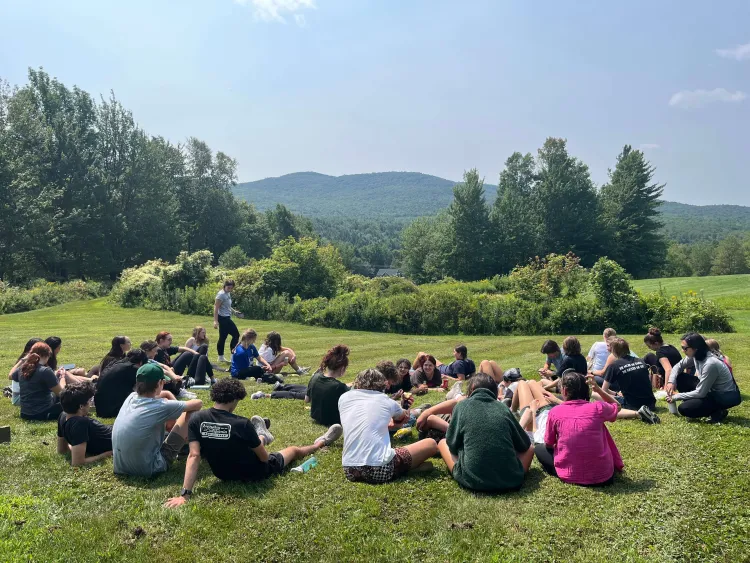 Students sit in a circle outside with a mountain visible in the background