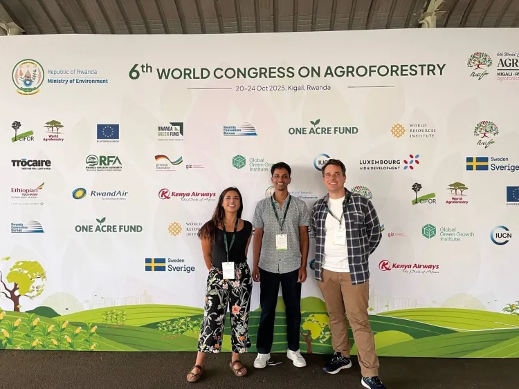 Three people stand in front of 6th World Congress of Agroforestry banner